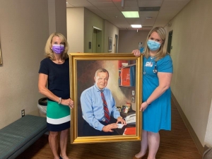 Sara Mayhew (left) and Mary Catherine Moree, M.D., pose with donated portrait of longtime family physician John Vetter, M.D.