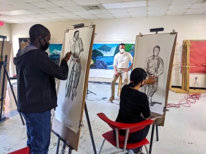 Richmond Community College art instructor Marcus Dunn sits on a stool and serves as a model for students to draw using charcoal.