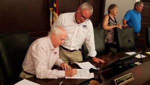 Rockingham City Manager Monty Crump stands over Mayor Steve Morris as he signs documents for a loan from the USDA during a special meeting Thursday night. The low-interest loan will help the city pay for the construction of a downtown campus for Richmond Community College.