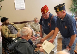 Jeff Joyner and Wayne Johnson present Sammy Lampley with with a flag and certificate of appreciation on behalf of the American Legion for his service in the military during a ceremony at Hamlet House on Monday. The American Legion made a Veterans Day presentation at Richmond Pines Health Care and Rehabilitation.